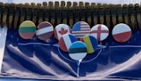 A series of metallic bullets are aligned together, creating an imposing backdrop. Below the bullets, several round badges display flags from different countries, including the United States, Canada, and others, arranged neatly on a NATO flag.