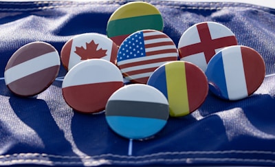 Several round badges featuring different national flags are laid out on a textured blue fabric surface.