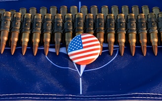 A row of bullets is arranged horizontally across a dark blue surface. In the center, there is a round button featuring the American flag design.