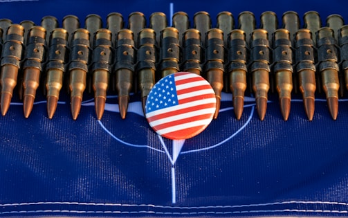 A row of bullets is arranged horizontally across a dark blue surface. In the center, there is a round button featuring the American flag design.