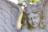 A stone sculpture of an angel with detailed feathered wings. The facial expression is serene, with half-closed eyes and a gentle smile. The soft lighting creates a calm and peaceful atmosphere, highlighting the texture of the stone.