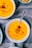 Bright orange creamy soup served in white bowls, topped with croutons and a sprinkle of black pepper, placed on a textured gray cloth.