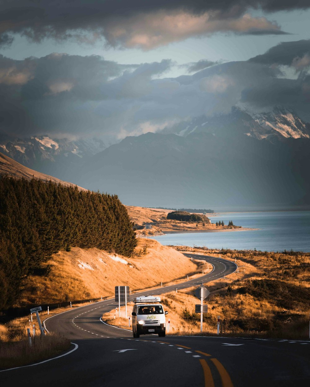 a van driving down a road next to a lake