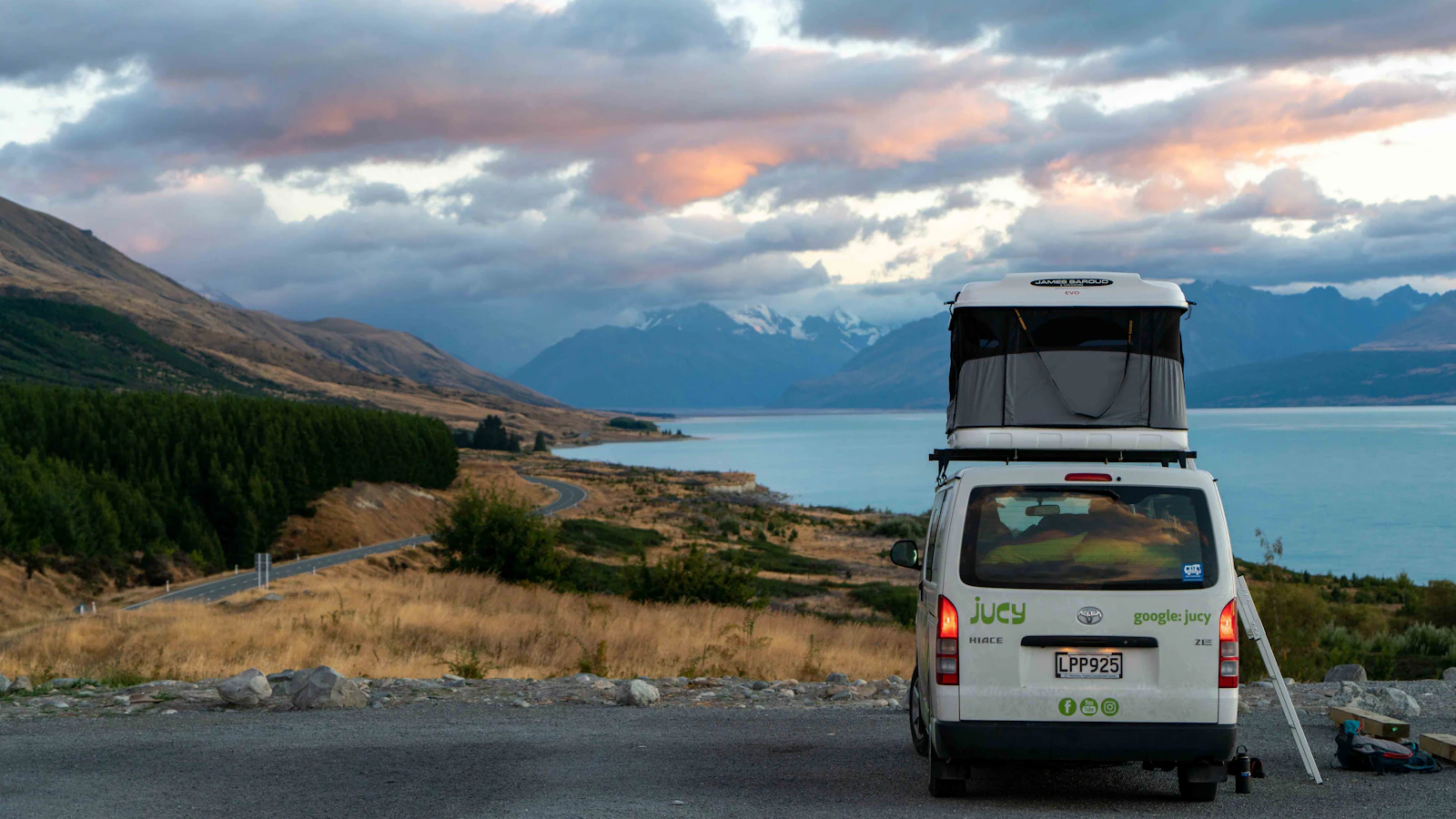 Camper van with a raised roof parked beside a lake and mountains