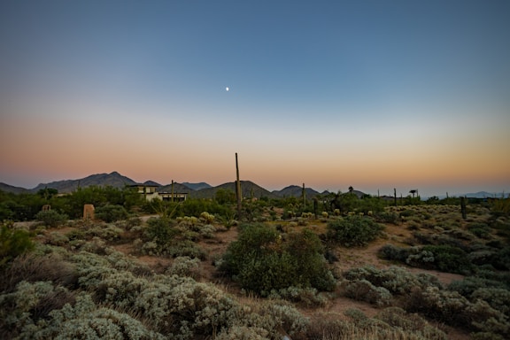 A peaceful desert landscape at sunset with a small off-grid cabin nestled among sagebrush and red rocks.