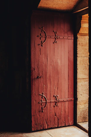 An old rustic wooden door with peeling paint and iron hinges, bathed in warm afternoon light.