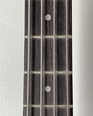 A close-up view of a guitar fretboard featuring four metallic strings and dot inlays on a wooden surface.