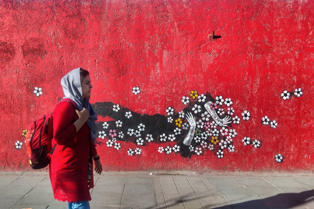 a woman walking past a red wall with a painting on it