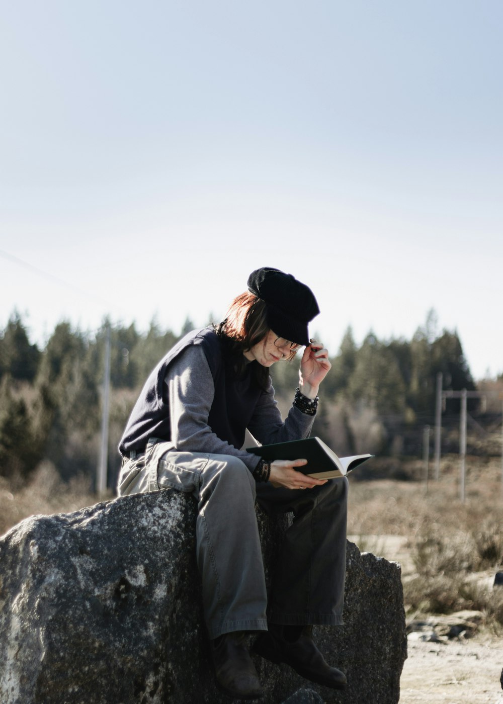 a woman sitting on a rock reading a book