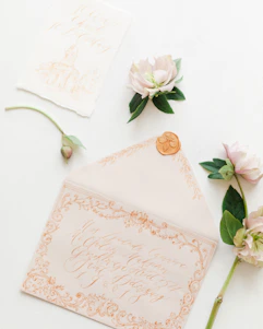 Close-up of delicate paper invitations with intricate hand-painted floral designs and textured finishes.
