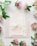 A set of elegant wedding invitations featuring intricate calligraphy and an illustration of a building sits atop an envelope. Surrounding the invitations, delicate flowers and green leaves add a touch of nature.