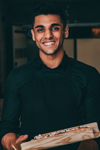 a man in a black shirt is holding a pizza