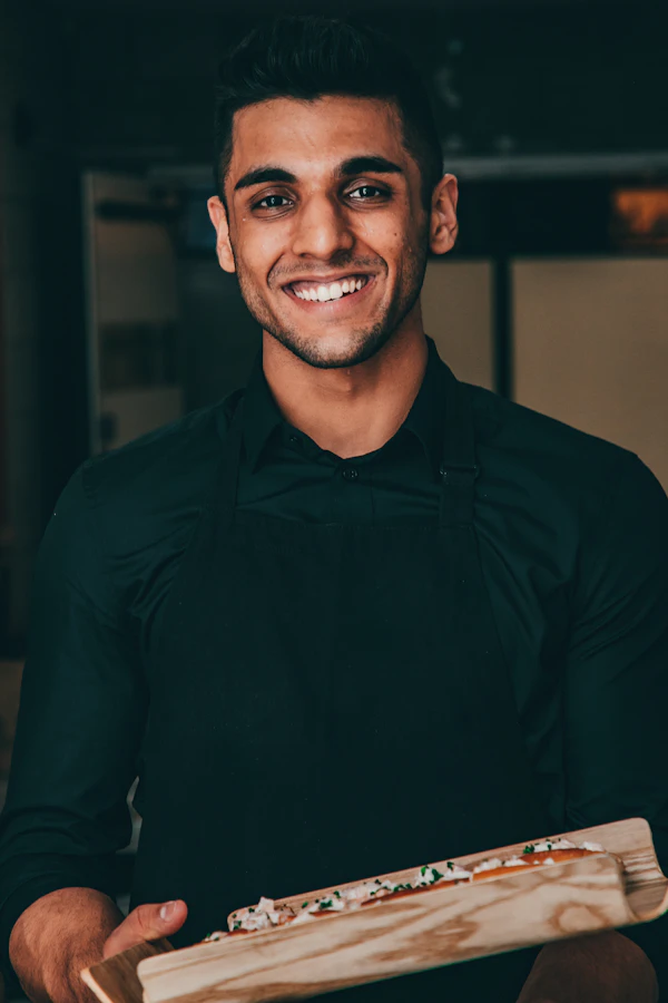 A pizzeria owner proudly holding a fresh pizza in his restaurant