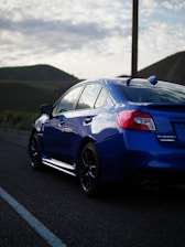 A sleek car parked on a rural road with rolling hills in the background.