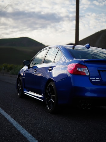 A compact blue car with clean lines, parked beside a green countryside road.