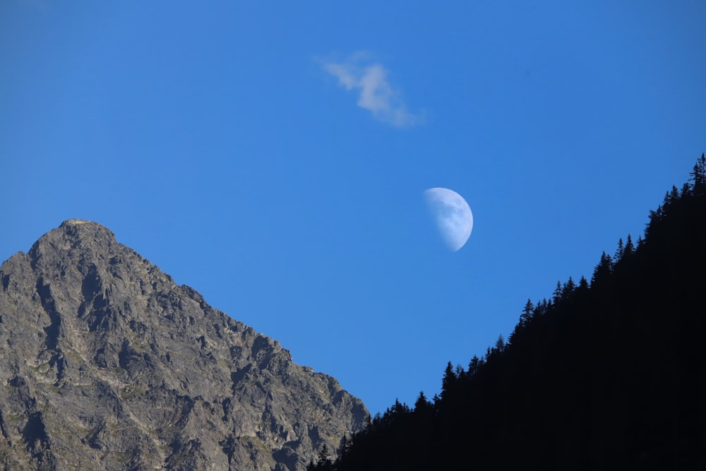 a half moon is seen in the sky above a mountain