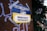 A poster on a wall, secured with duct tape, features the Ukrainian flag's blue and yellow colors and reads 'Solidarity is now for Ukraine'. It includes a call for donations to 'savethechildren.ch' and a QR code. The background has graffiti on a brown surface and there are plants with flowers on the right.