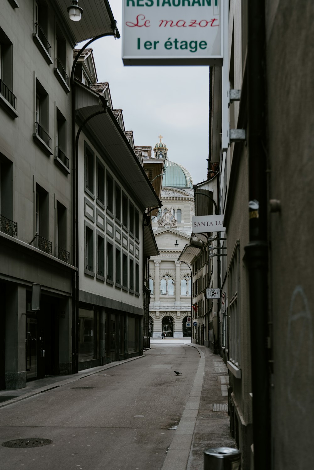 a narrow street with a restaurant sign hanging from the side of it