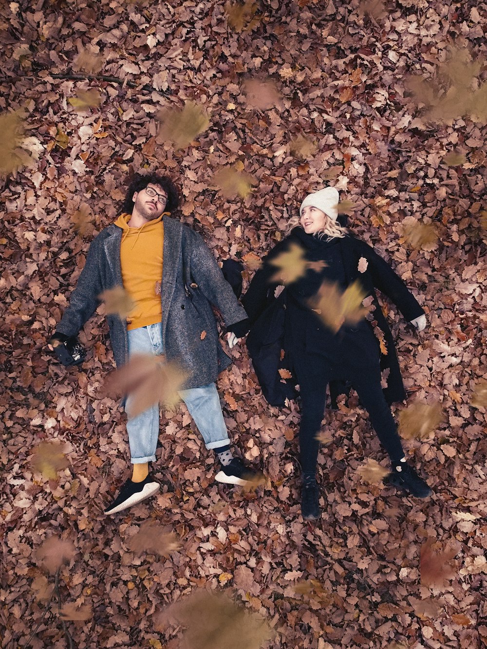 a couple of people laying on top of a pile of leaves
