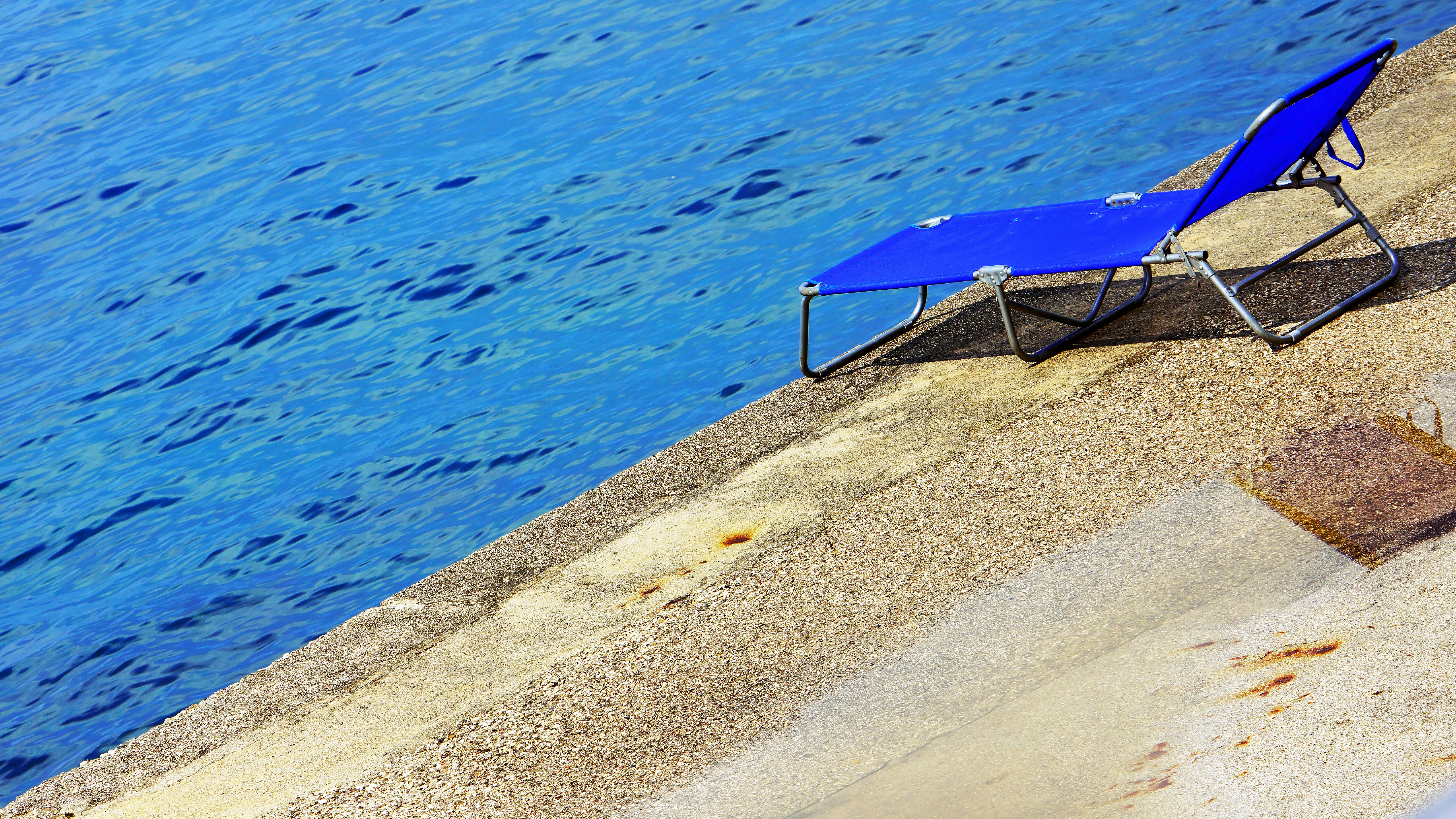 A blue lawn chair sitting next to a body of water photo – Free Blue ...