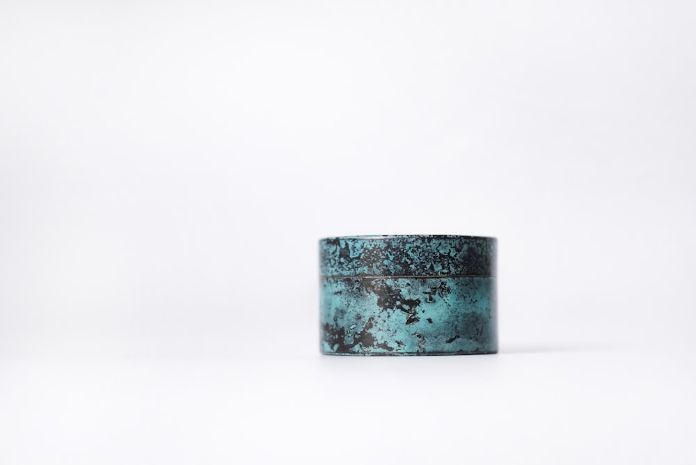 a teal colored metal container sitting on a white surface