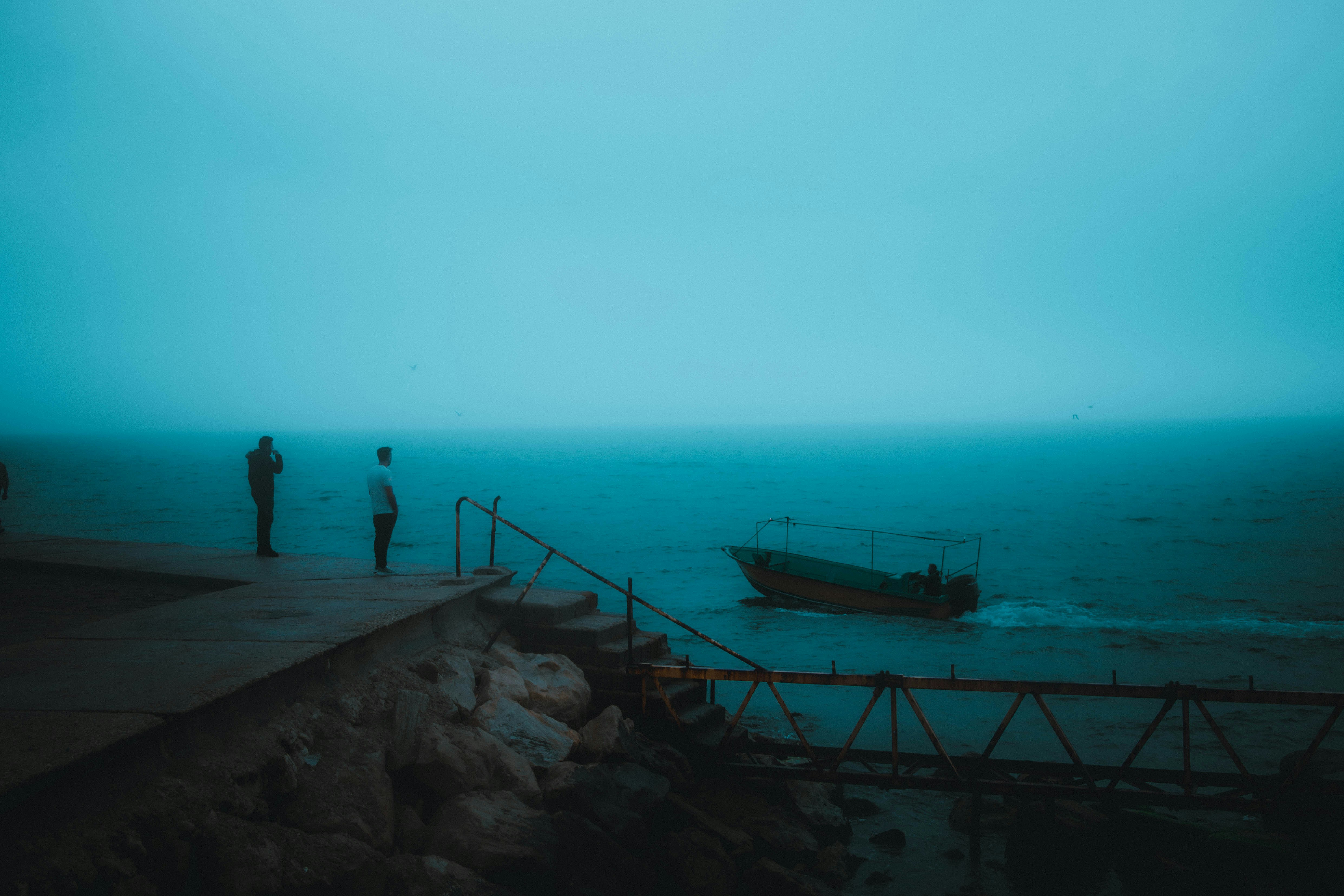 Un paio di persone in piedi sulla cima di una spiaggia accanto a una barca
