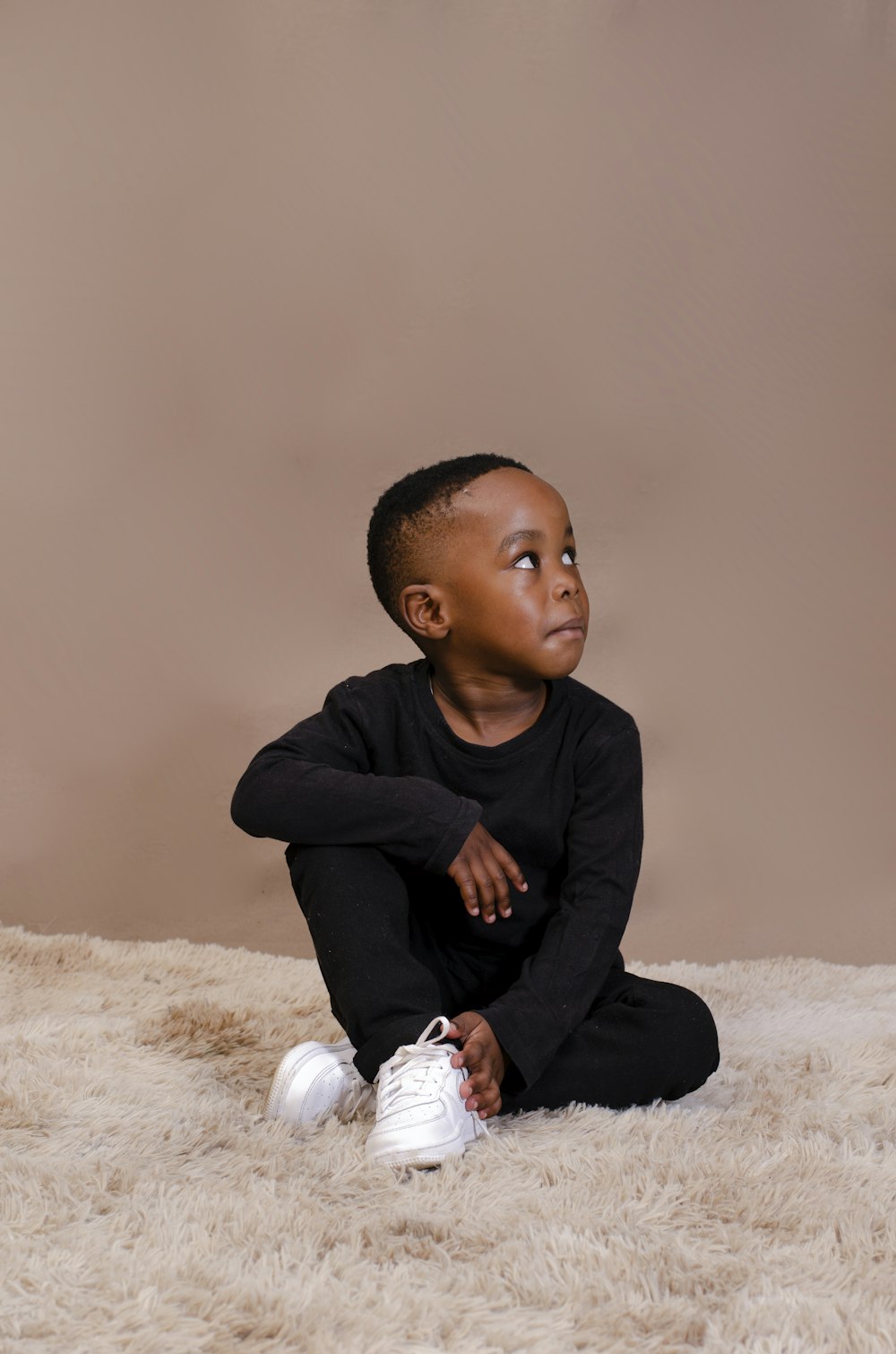 a young boy sitting on a fluffy white carpet