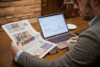 a man reading a newspaper while using a laptop