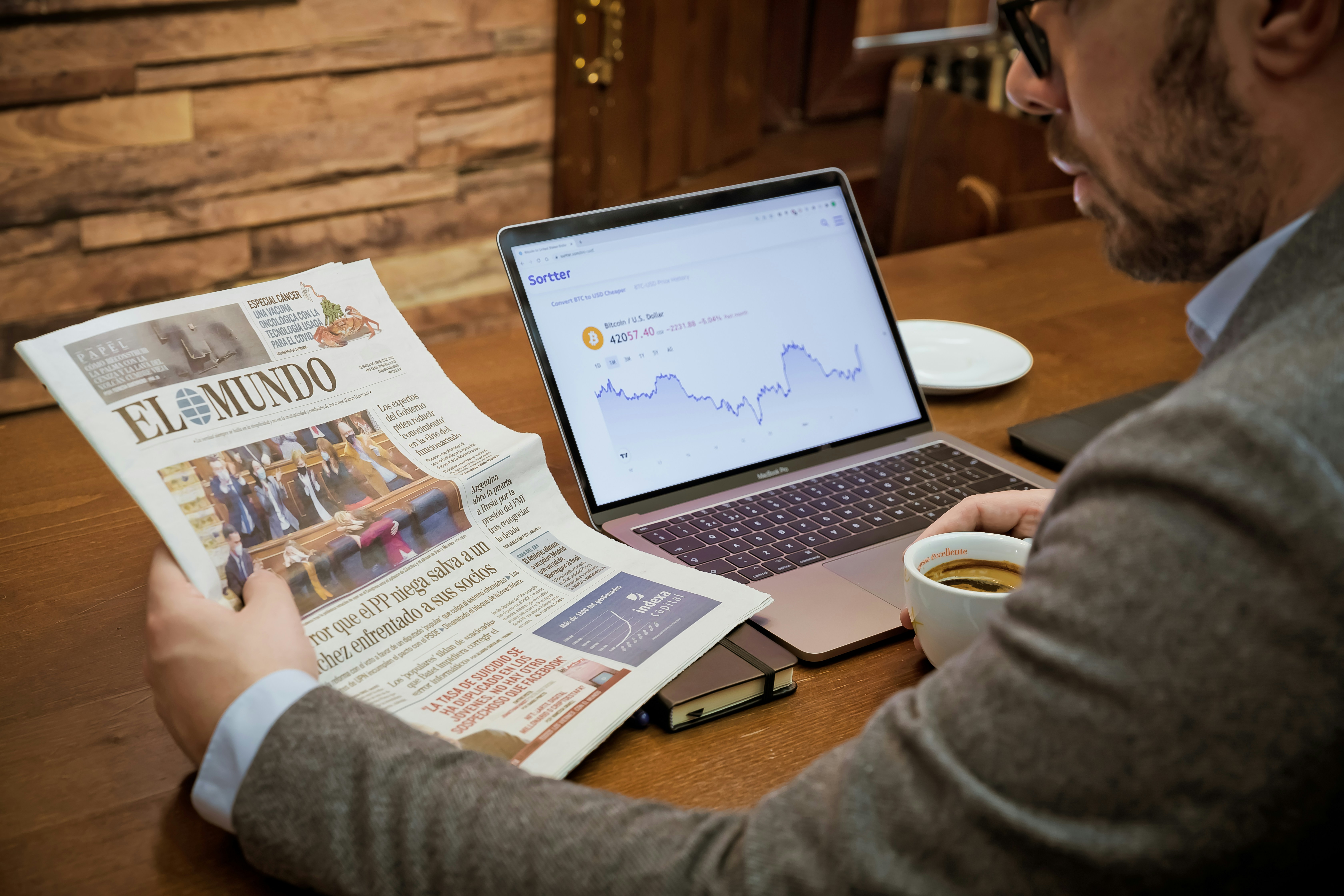 Drinking coffee in a coffee shop checking El Mundo from Spain with Bitcoin chart aside.