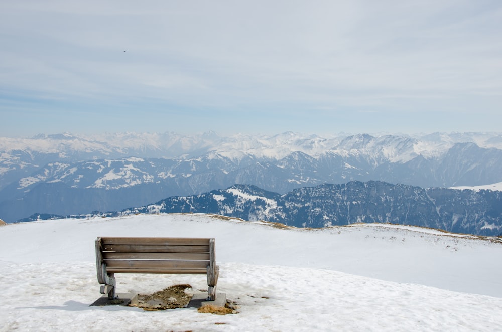 um banco de madeira sentado em cima de uma encosta coberta de neve