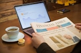 a person reading a newspaper next to a laptop computer
