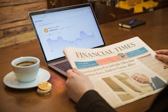 a person reading a newspaper next to a laptop computer