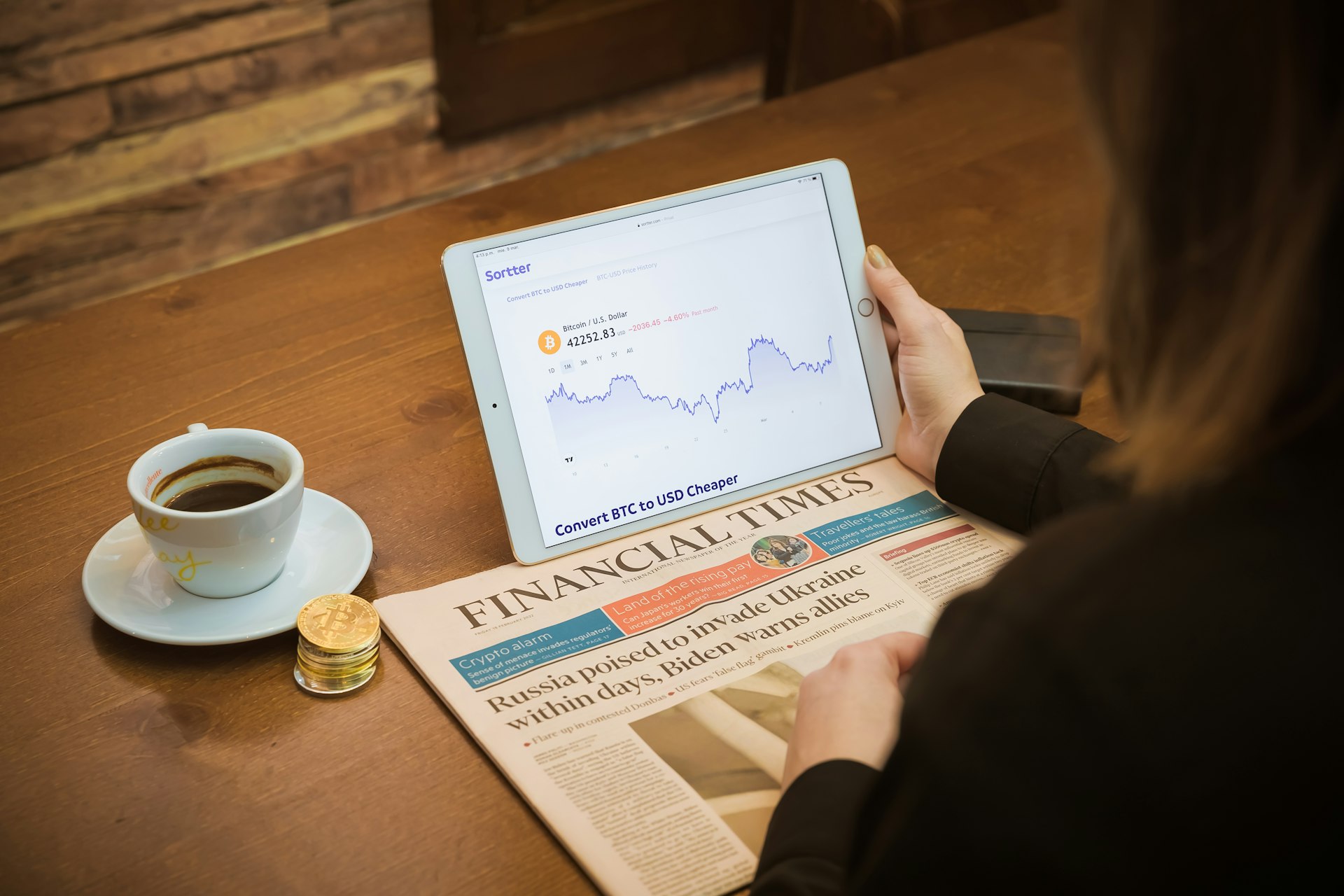 A woman reviewing market charts on a laptop alongside a financial newspaper