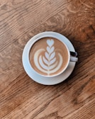 A steaming cup of coffee with latte art served on a minimalist ceramic saucer.