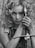 A woman with curly hair holds a sword vertically close to her face. Her expression is intense and focused. The image is black and white, adding a dramatic and timeless feel.