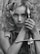 A woman with curly hair holds a sword vertically close to her face. Her expression is intense and focused. The image is black and white, adding a dramatic and timeless feel.