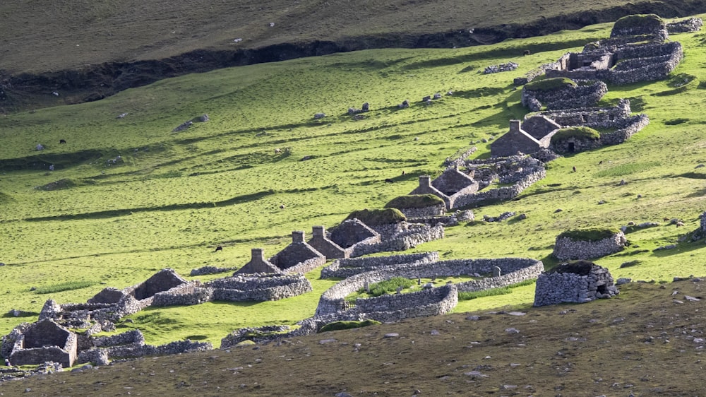 a grassy field with a stone wall and a hill in the background