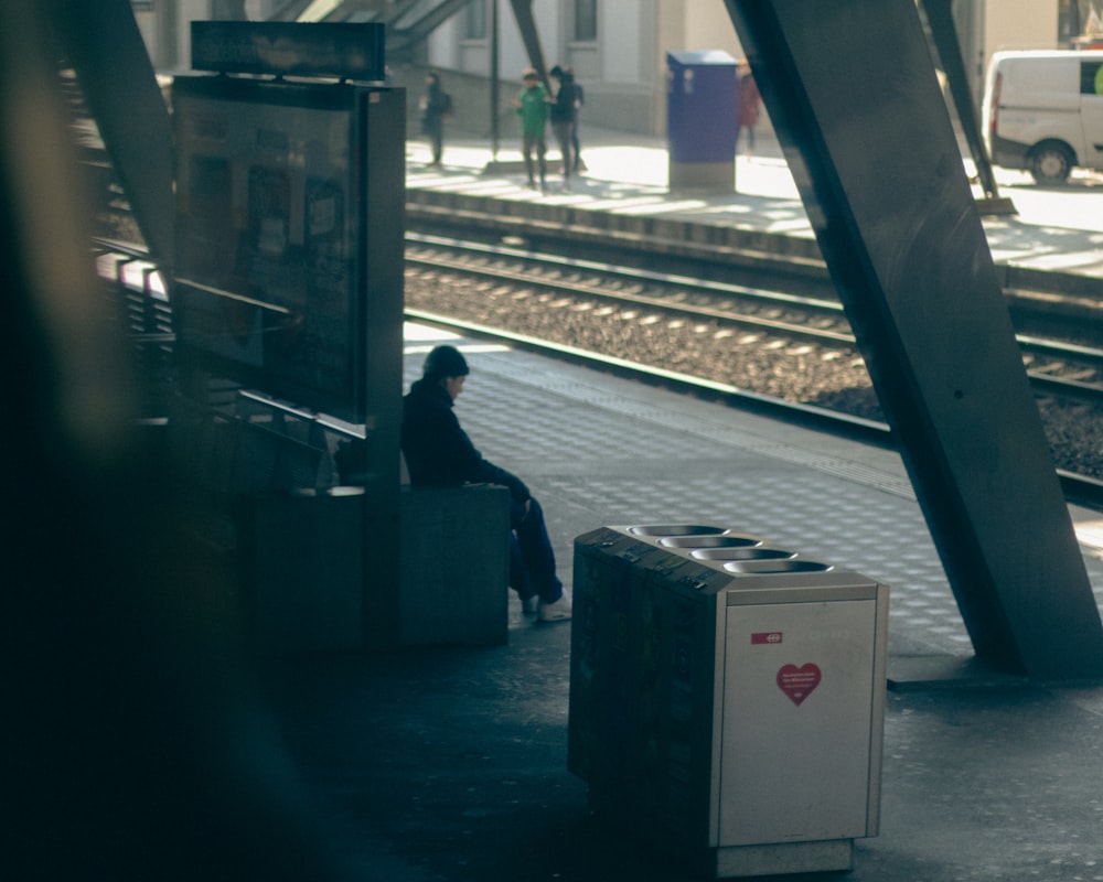 a person sitting on a bench next to a train track