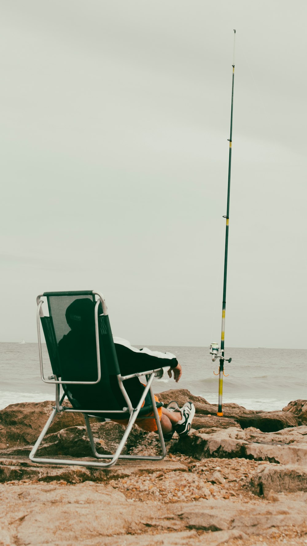 a man sitting in a chair on the beach next to a fishing pole