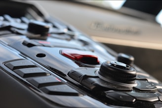 Close-up of a vehicle's control panel featuring buttons and a central control knob. The design is sleek and modern, with a mix of polished and matte surfaces, reflecting an advanced technological style.