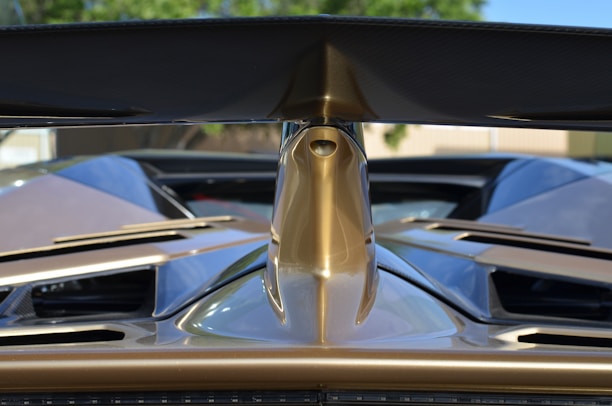 Close-up of a sleek, glossy car spoiler catching the sunlight on a winding road.