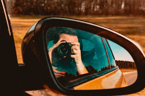 a man taking a picture of himself in the side mirror of a car