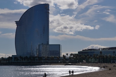 people are walking on the beach in front of a tall building