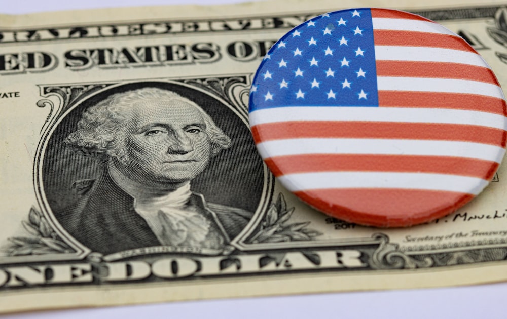 Un billete de un dólar y un botón con la bandera estadounidense