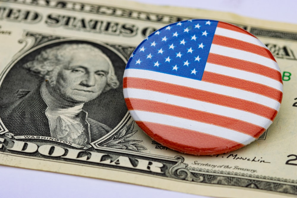 a button with the american flag on it sitting on top of a hundred dollar bill
