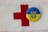 A red cross symbol is printed on a white fabric background. Next to it is a circular badge with the Ukrainian coat of arms in blue on a yellow background.
