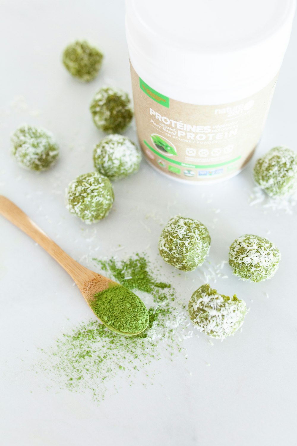 a wooden spoon filled with green powder next to a jar of powdered sugar