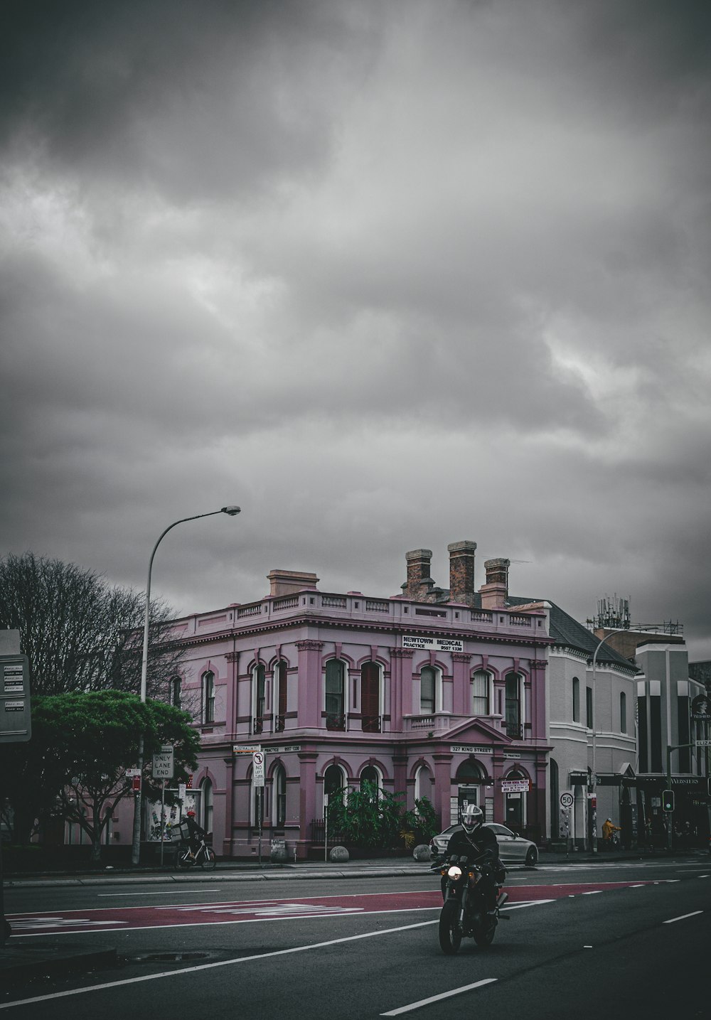 a man riding a motorcycle down a street next to a tall pink building