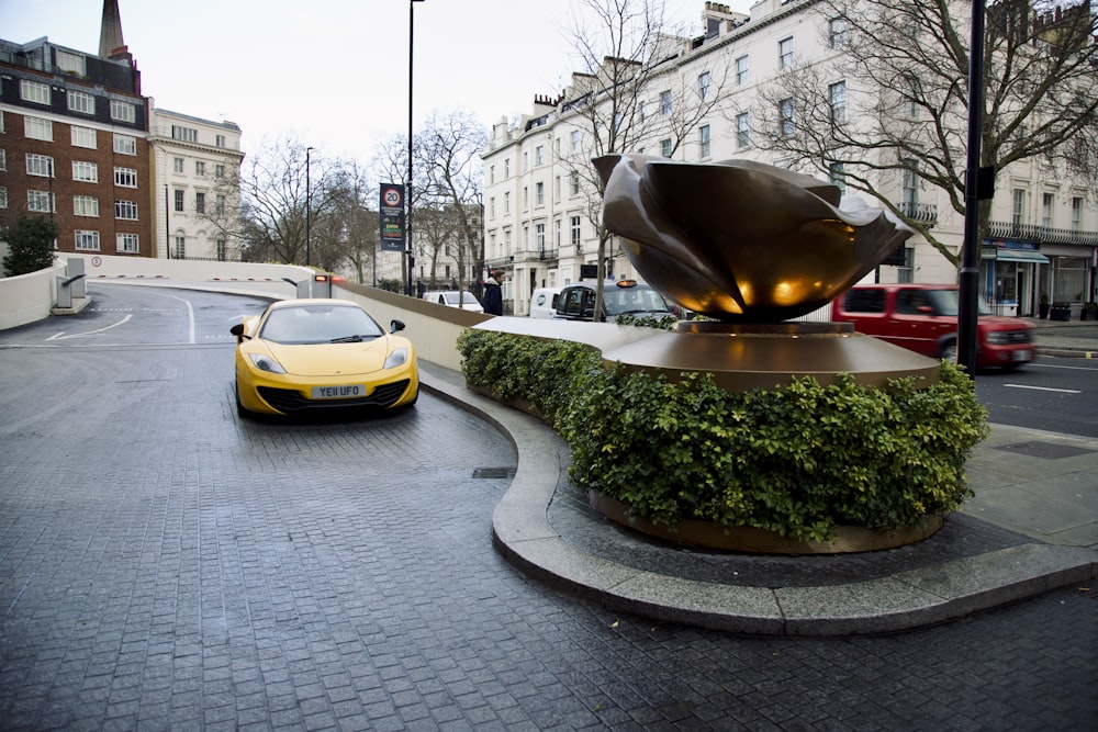 a yellow sports car parked in front of a statue