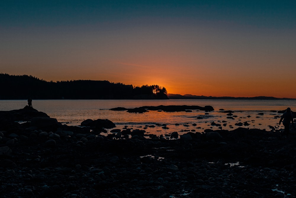 Eine Person, die bei Sonnenuntergang an einem felsigen Strand steht